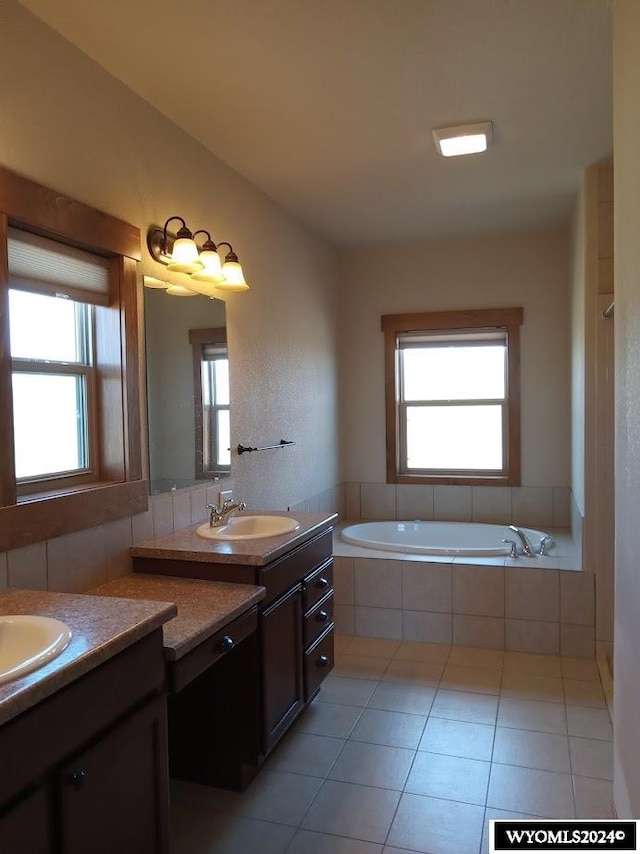 bathroom featuring tile patterned floors, plenty of natural light, a relaxing tiled tub, and vanity