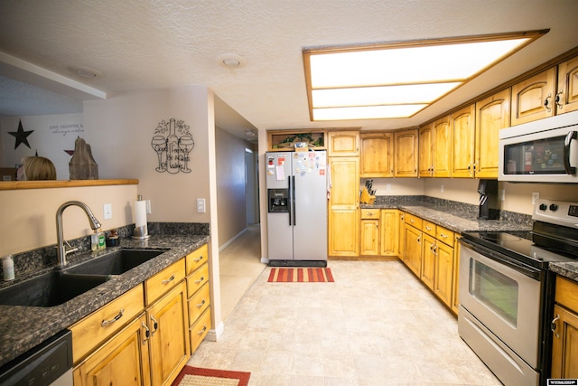 kitchen with dark stone counters, stainless steel appliances, a textured ceiling, and sink