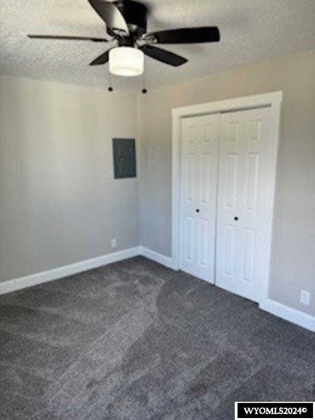 unfurnished bedroom featuring a closet, a textured ceiling, dark carpet, ceiling fan, and electric panel