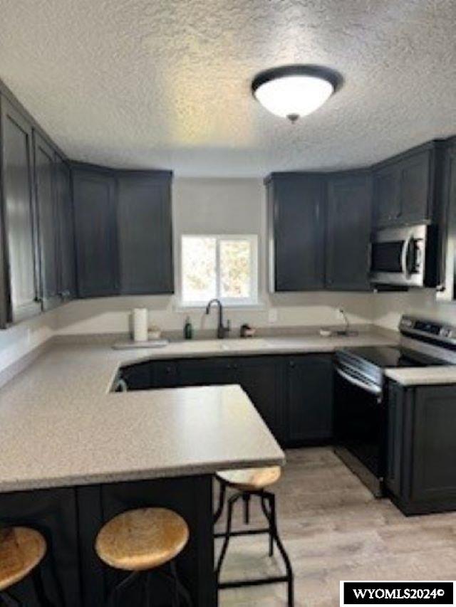 kitchen featuring a textured ceiling, appliances with stainless steel finishes, kitchen peninsula, and a breakfast bar