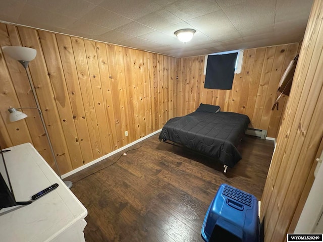 bedroom with wooden walls, baseboard heating, and dark wood-type flooring