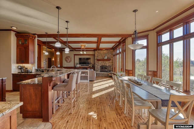 dining space with a stone fireplace, crown molding, beam ceiling, light hardwood / wood-style flooring, and sink