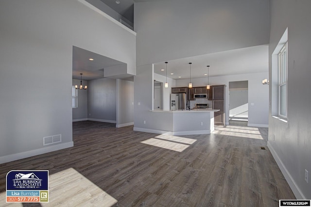 unfurnished living room featuring a notable chandelier, a towering ceiling, and dark hardwood / wood-style flooring