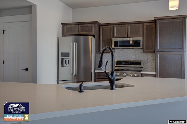 kitchen with sink, tasteful backsplash, dark brown cabinets, appliances with stainless steel finishes, and light stone countertops