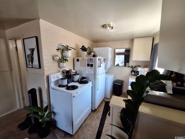 kitchen with washer / clothes dryer, white appliances, white cabinetry, and brick wall