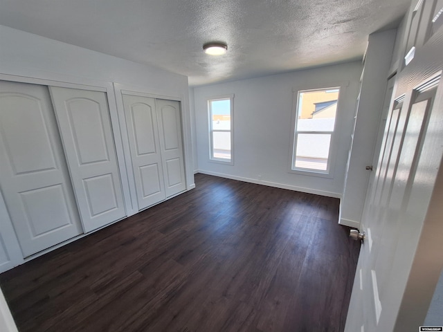 unfurnished bedroom with multiple closets, dark hardwood / wood-style floors, and a textured ceiling