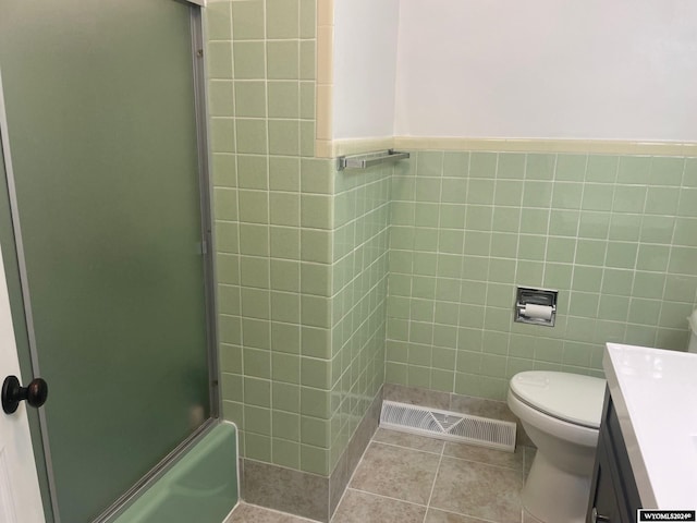 full bathroom with tile walls, vanity, toilet, and bath / shower combo with glass door