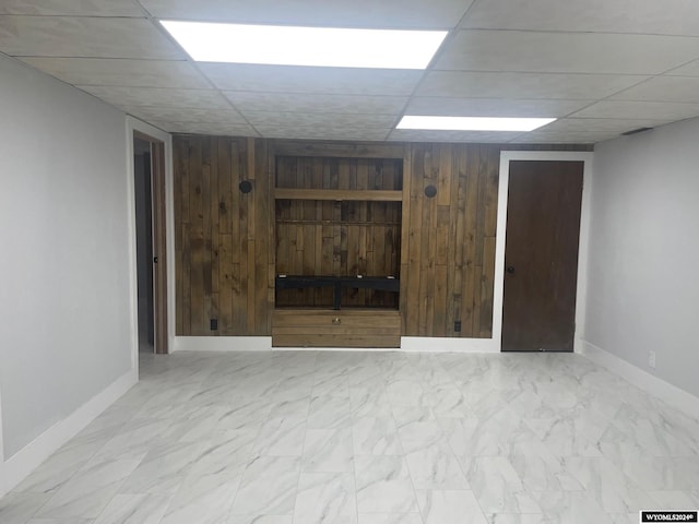 basement featuring a paneled ceiling and wooden walls