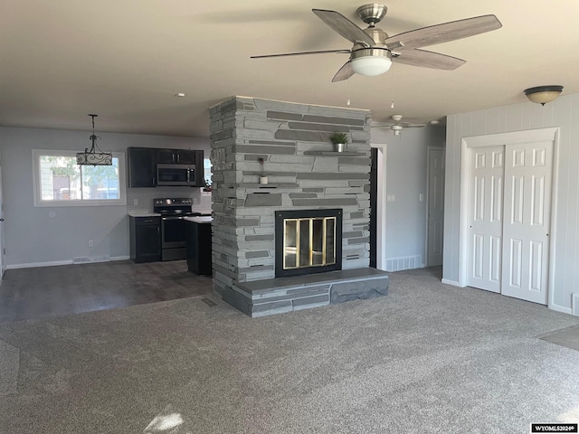 unfurnished living room featuring dark carpet, ceiling fan with notable chandelier, and a fireplace