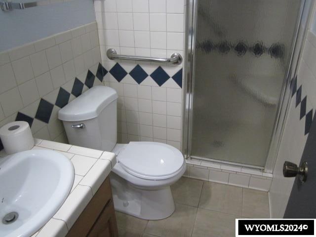 bathroom featuring vanity, tile patterned floors, walk in shower, tile walls, and toilet