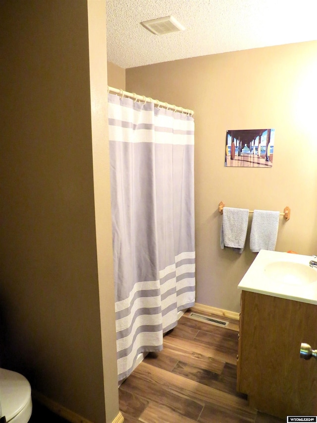 bathroom with vanity, curtained shower, wood-type flooring, a textured ceiling, and toilet