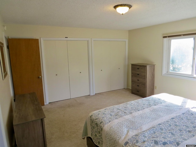 bedroom featuring light carpet, a textured ceiling, and two closets