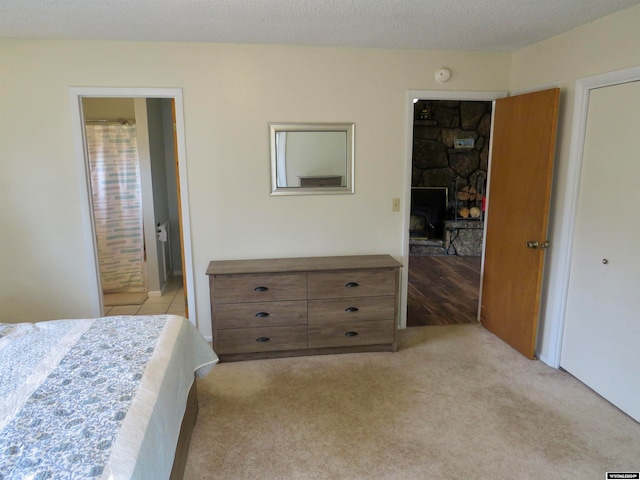 bedroom with a textured ceiling, a fireplace, ensuite bath, and light colored carpet