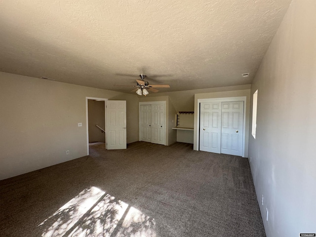 unfurnished bedroom with ceiling fan, two closets, carpet, and a textured ceiling