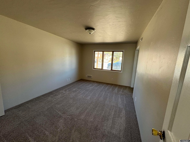 spare room featuring dark colored carpet and a textured ceiling