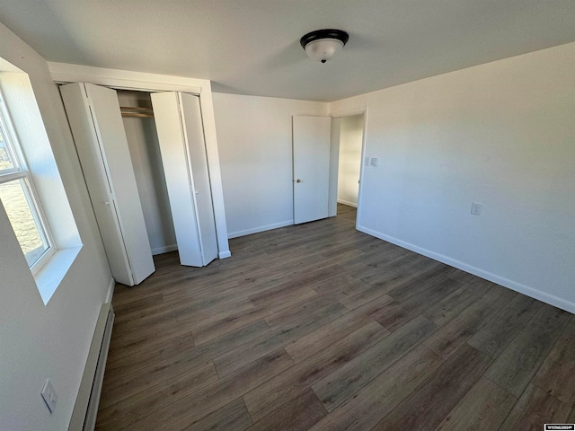 unfurnished bedroom with a baseboard radiator, a closet, and dark hardwood / wood-style flooring