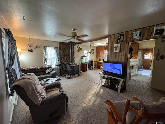 living room with light colored carpet, a wood stove, ceiling fan, and wooden walls