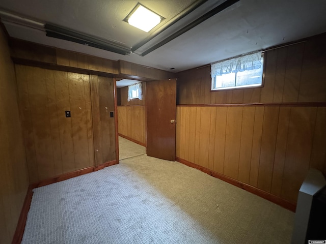 basement featuring a wealth of natural light, light colored carpet, and wood walls