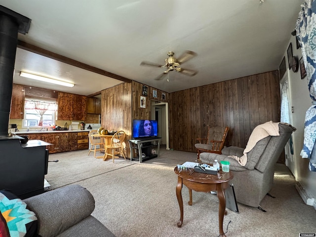 carpeted living room featuring a wood stove, wooden walls, and ceiling fan