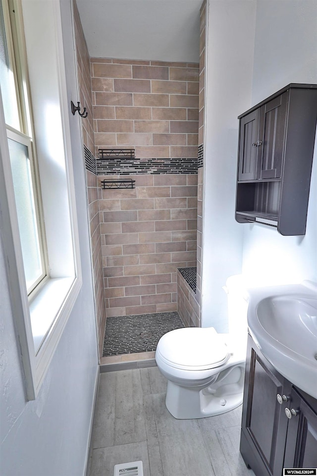 bathroom with tiled shower, vanity, and toilet