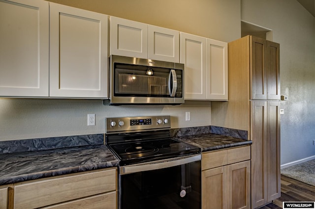 kitchen with light brown cabinetry, stainless steel appliances, dark hardwood / wood-style floors, and dark stone countertops