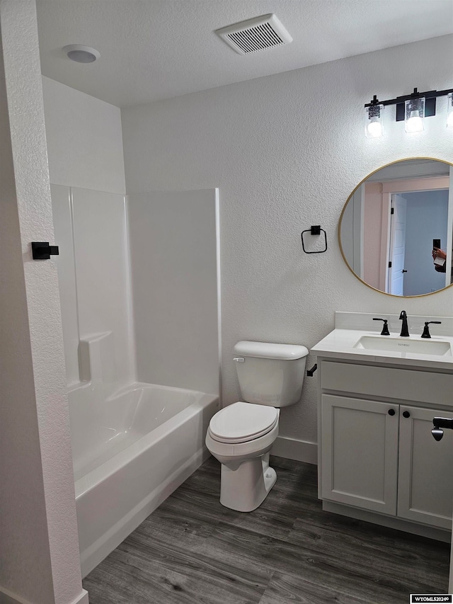 full bathroom featuring vanity, wood-type flooring, a textured ceiling, washtub / shower combination, and toilet