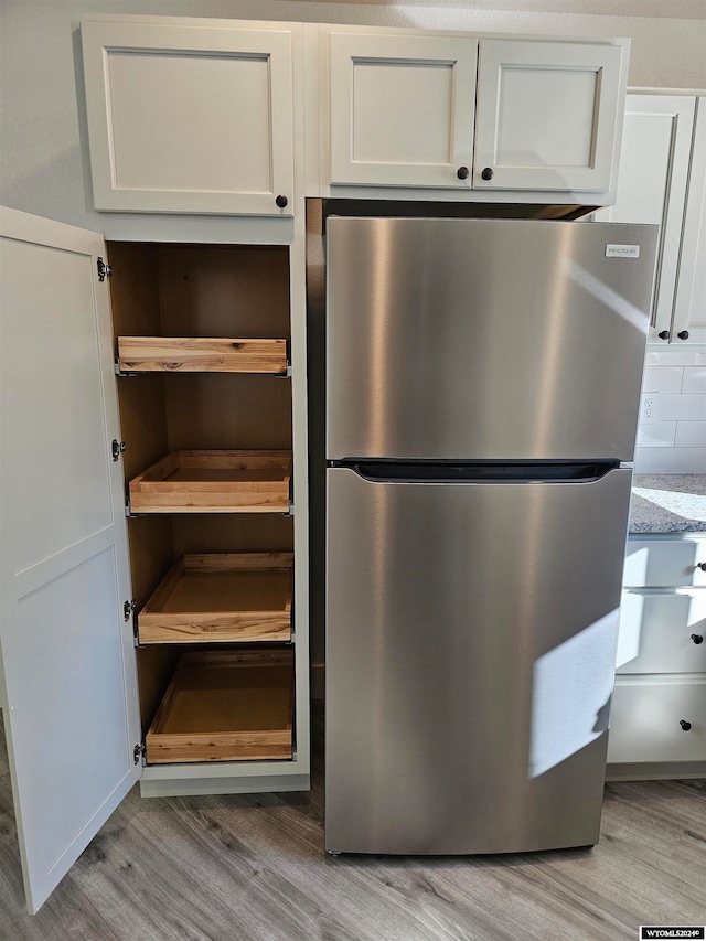 room details featuring light wood-type flooring, stainless steel fridge, and white cabinetry