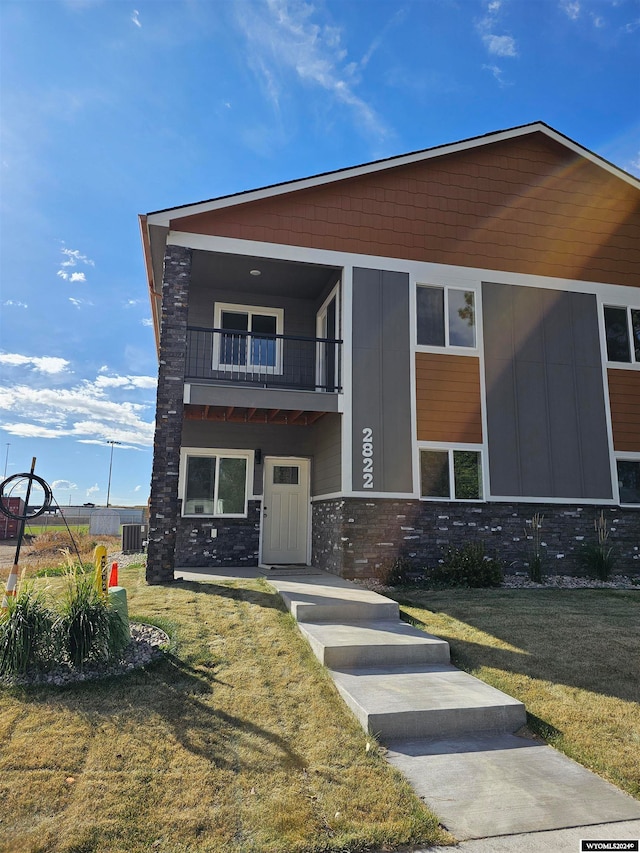 view of front of home with a balcony, a front lawn, and central AC