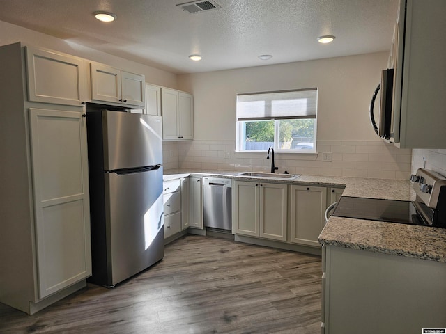 kitchen featuring light stone countertops, decorative backsplash, wood-type flooring, sink, and appliances with stainless steel finishes