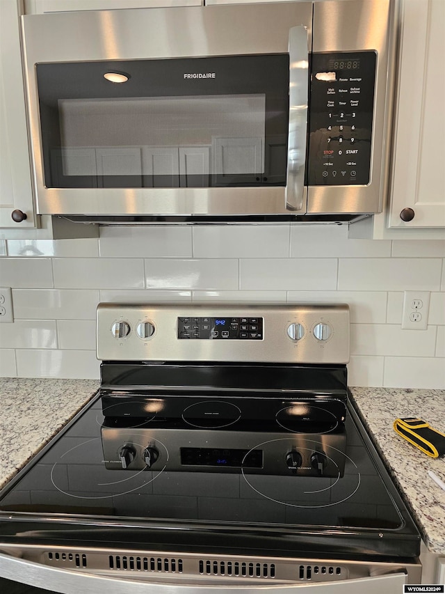 kitchen featuring stainless steel appliances, decorative backsplash, light stone counters, and white cabinetry