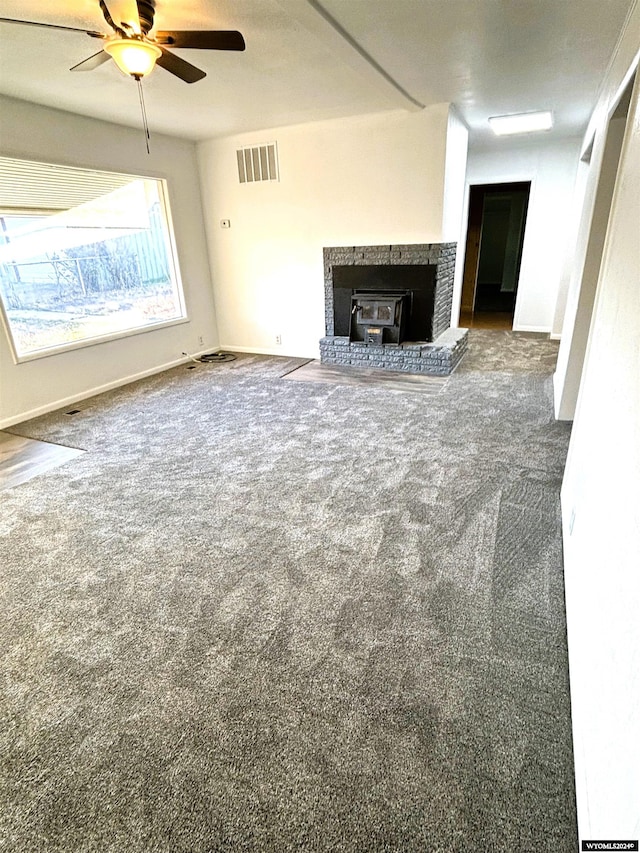 unfurnished living room with ceiling fan, carpet, and a wood stove