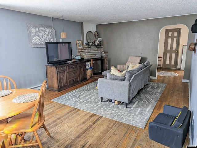 living room featuring a stone fireplace, a textured ceiling, and hardwood / wood-style floors