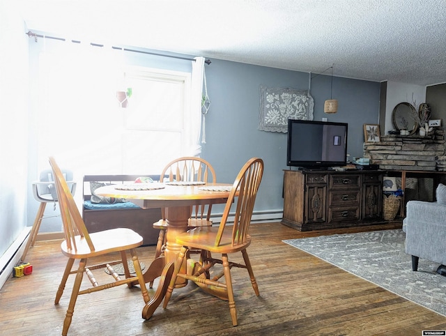 dining space featuring baseboard heating, hardwood / wood-style floors, and a textured ceiling