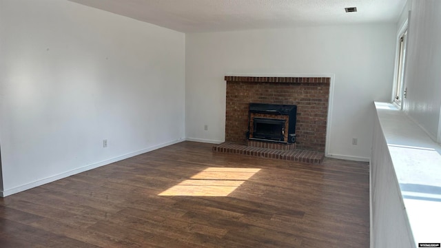 unfurnished living room featuring a textured ceiling, dark hardwood / wood-style flooring, and a brick fireplace