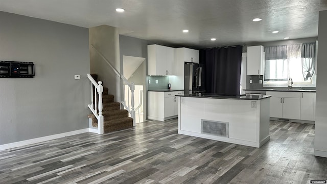 kitchen featuring sink, stainless steel fridge, a kitchen island, and white cabinets