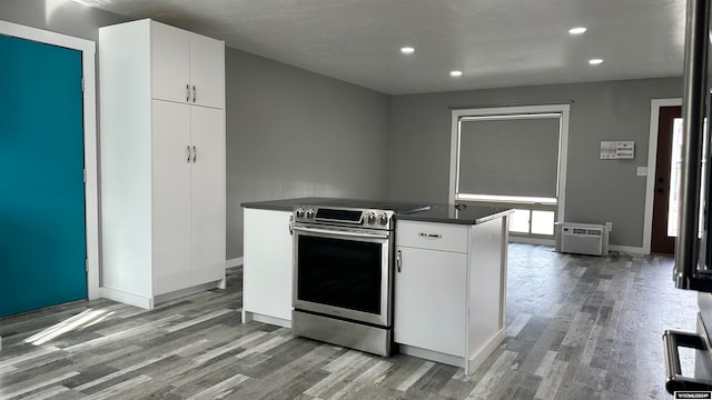 kitchen featuring hardwood / wood-style floors, a wall mounted AC, stainless steel range with electric cooktop, white cabinetry, and a center island