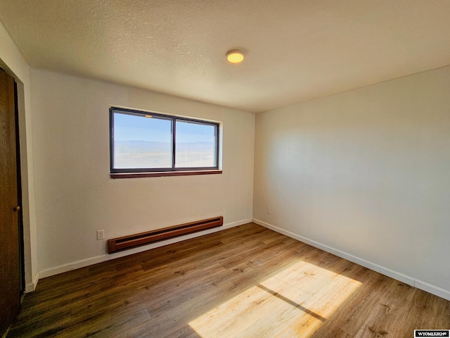 spare room with a textured ceiling, hardwood / wood-style flooring, and a baseboard radiator