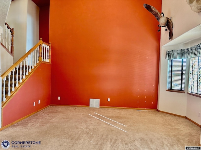 spare room featuring visible vents, a towering ceiling, stairs, baseboards, and carpet