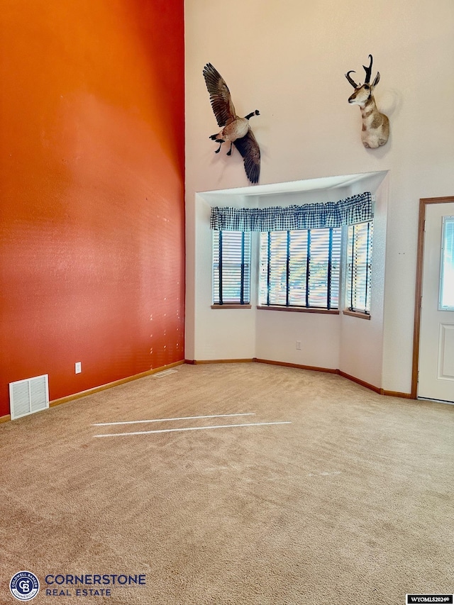 spare room featuring a towering ceiling, carpet, visible vents, and baseboards