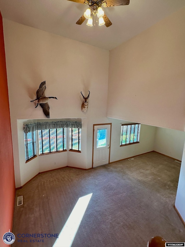 empty room with carpet floors, visible vents, a towering ceiling, and a ceiling fan