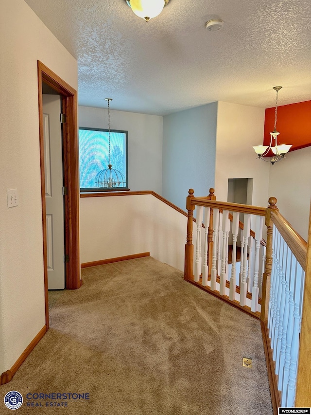 hallway with carpet, a textured ceiling, an upstairs landing, and an inviting chandelier