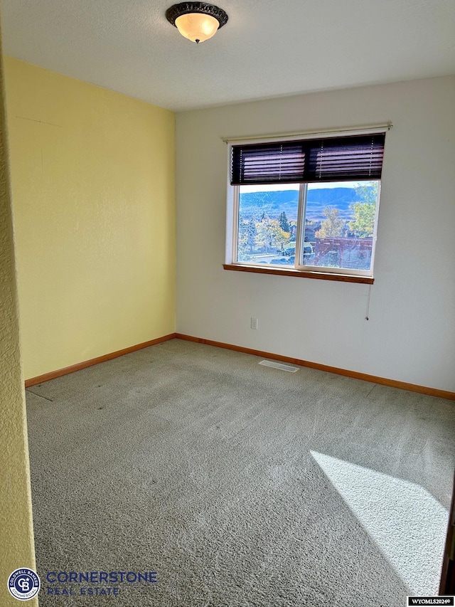 carpeted spare room with baseboards, visible vents, and a textured ceiling