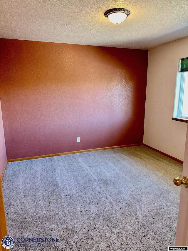 carpeted empty room featuring a textured ceiling and baseboards