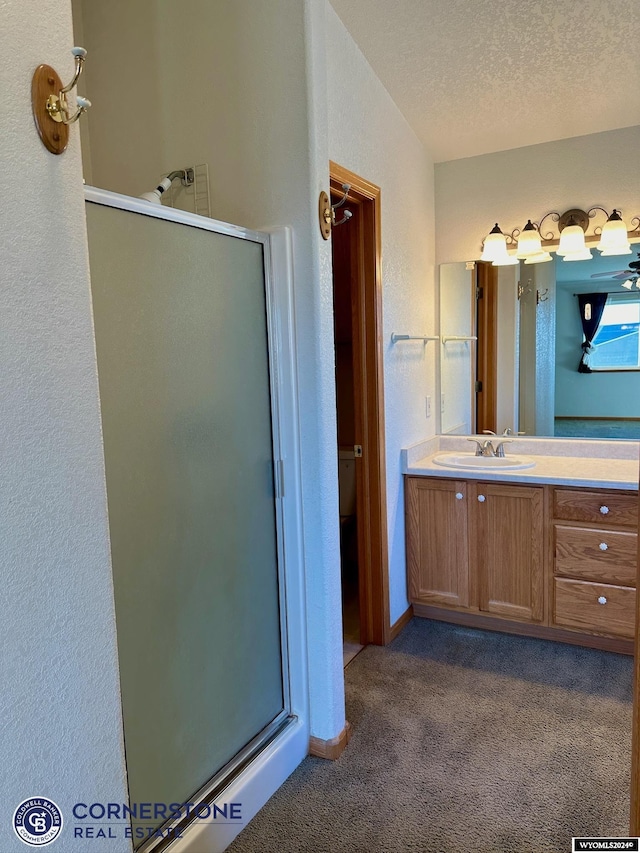 bathroom with a textured ceiling, a textured wall, a stall shower, and vanity