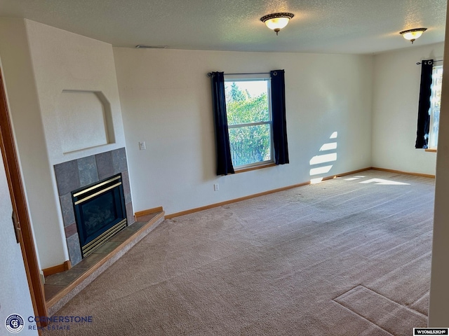 unfurnished living room with a textured ceiling, carpet floors, a tile fireplace, and baseboards