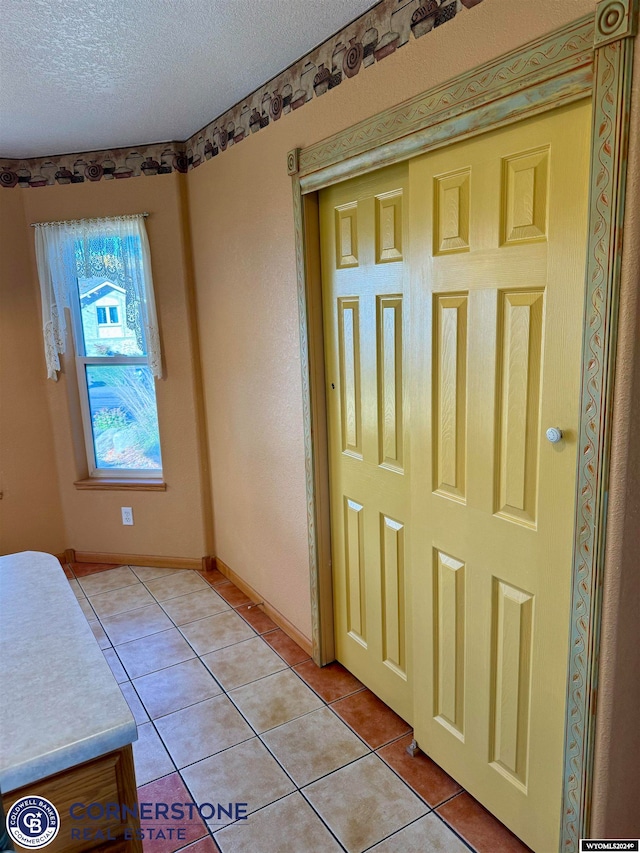 doorway with light tile patterned floors, baseboards, and a textured ceiling