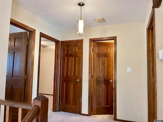 corridor featuring a textured ceiling and light colored carpet