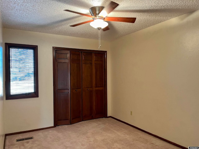 unfurnished bedroom with a closet, a textured ceiling, light colored carpet, and ceiling fan