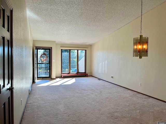 carpeted empty room with a textured ceiling and an inviting chandelier