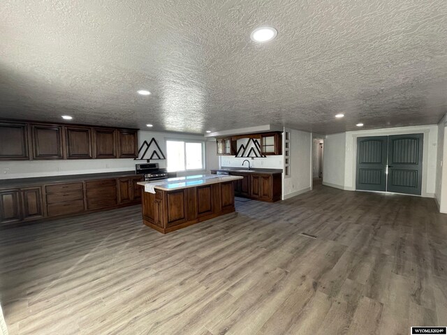 kitchen featuring wood-type flooring, sink, a textured ceiling, a center island, and stainless steel stove